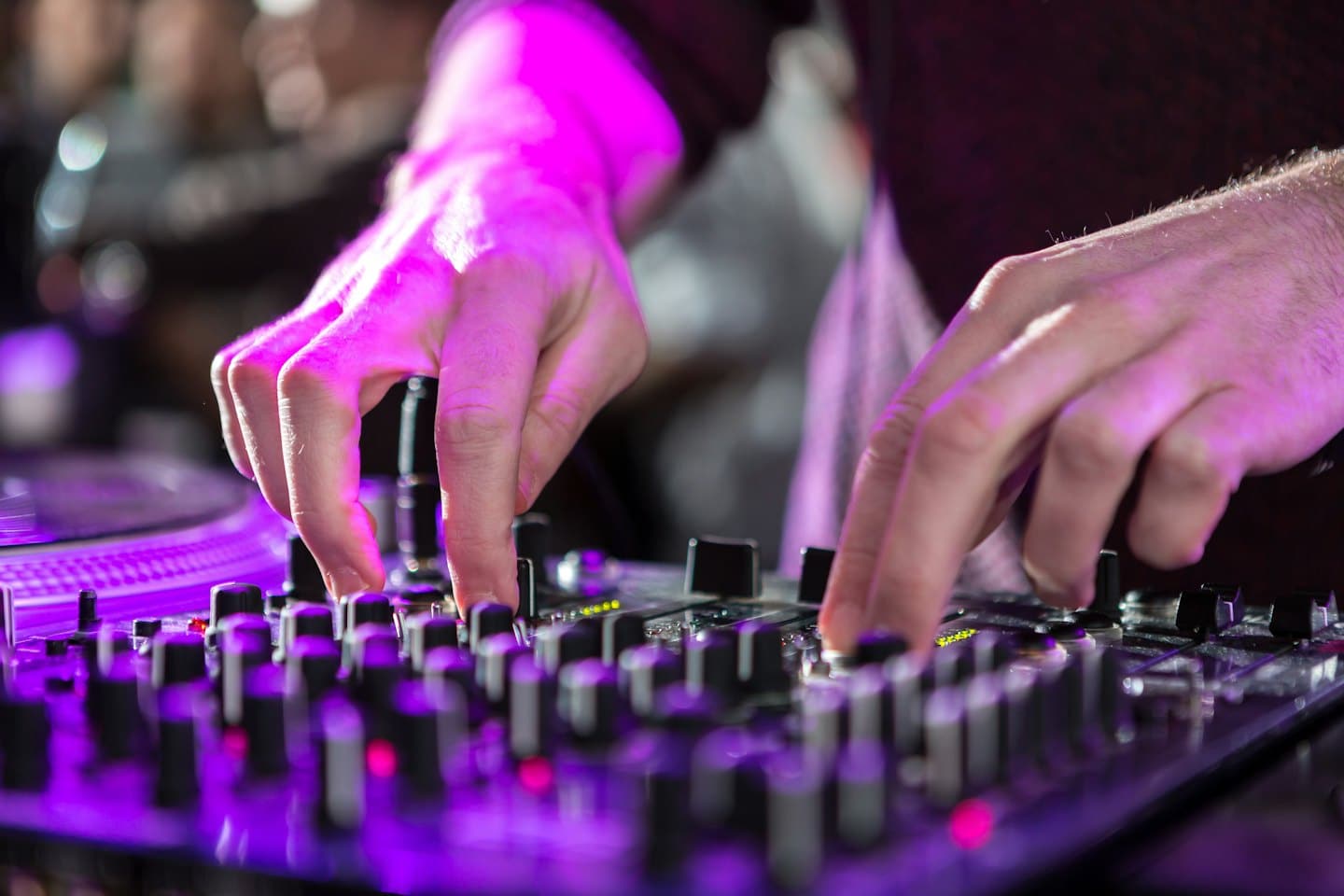 Hände eines DJs, die Regler an einem Mischpult und Plattenspieler einstellen.